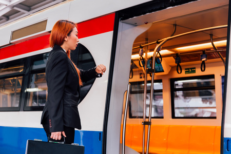 Young Asian businesswoman in formal suit waiting for train to arrive and looking at watch to check time for avoid late at workの写真素材