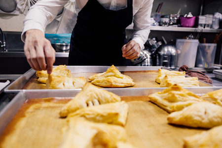 Close-up of chef in apron baking and making many handmade breads on tray freshly baked from over in kitchen for commercial bakery shopの写真素材