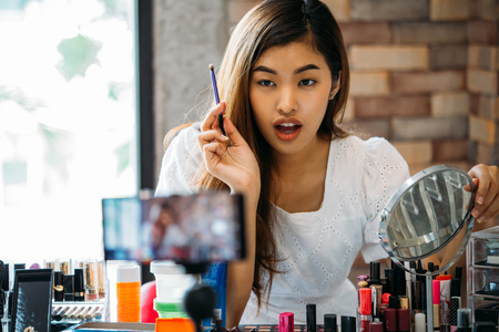 Pretty Asian woman recording makeup tutorial video about cosmetics with mobile phone on tripodの写真素材