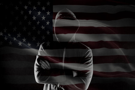 Double exposure of concept of criminal in USA with silhouette of male with crossed hands in hood and...
