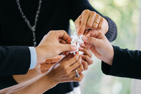 Hands of anonymous people joining pieces of white jigsaw puzzle in officeの写真素材