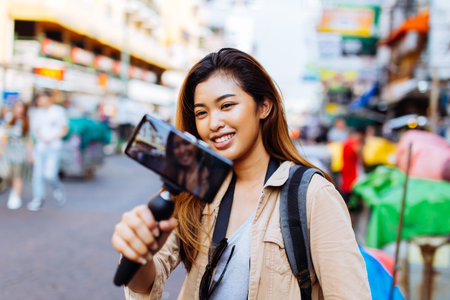 Young Asian female tourist woman holding a gimbal with smartphone and recording videos for blog. Travel blogger and vlogger conceptの写真素材