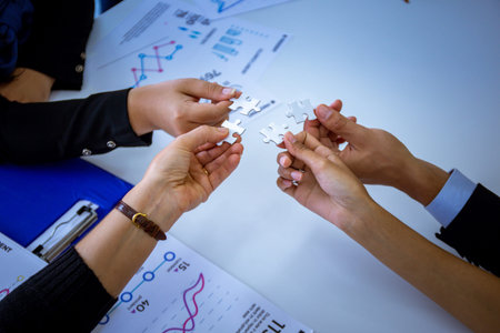Hands of anonymous people joining pieces of white jigsaw puzzle in office