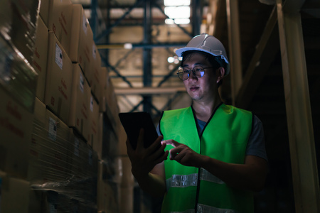 Young Asian male warehouse worker using a digital tablet inside warehouse to check inventory and stock management in factoryの写真素材