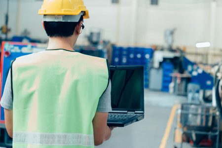 Asian male Industrial engineer in hardhat works with laptop in safety jacket at heavy industry...