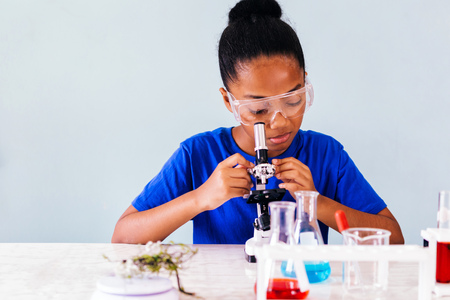 Young African American kid using microscope and experimenting scientific lab along with chemical substance tubes and flasks in classroomの写真素材