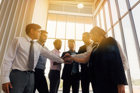 From below of multiethnic business men and women stacking hands together while standing in office in back litの写真素材