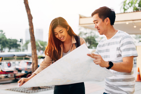 Traveling Asian woman and man reading map on street of Bangkok exploring city together, Thailandの写真素材