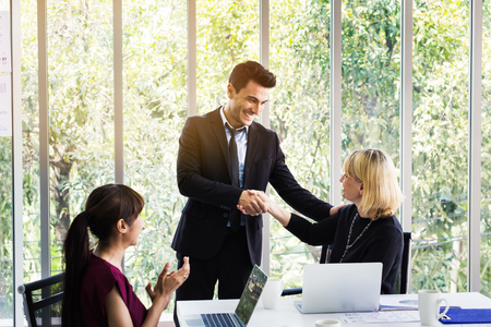 Business man and business woman shaking hands on meeting while female colleagues applauding in officeの写真素材
