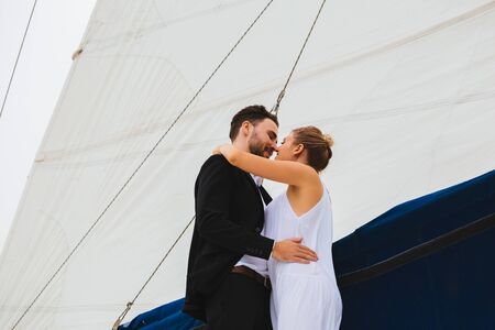 Handsome man and attractive woman smiling and kissing embracing on yacht in bright dayの写真素材