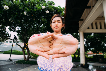 Asian female with closed eyes doing warm up exercise for arms during outdoor workout in city park