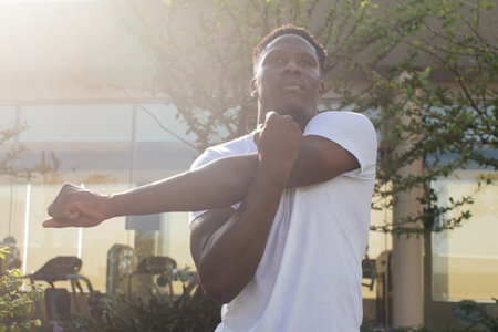 Portrait of African American man stretching arms in the city street. Young male fitness guy doing...