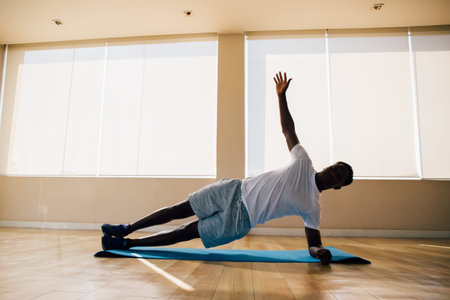 Athletic African American man balancing on one arm while doing side plank exercise on mat in gym