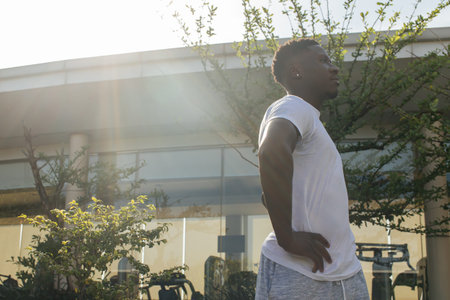Side view of African American sportsman in white t-shirt standing with hands on hips and resting...