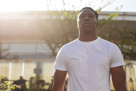 Back in lit muscular young African American man in white t-shirt training outdoors by gym in summer...