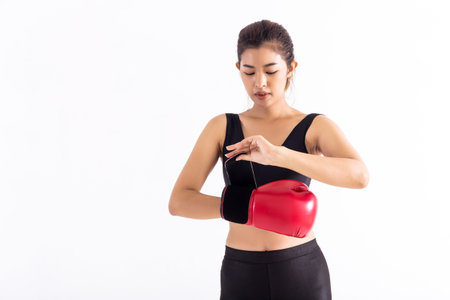 Fit Asian woman putting on red boxing gloves before boxing workout on white background. Young sportswoman fixing on hand red leather glove.の写真素材