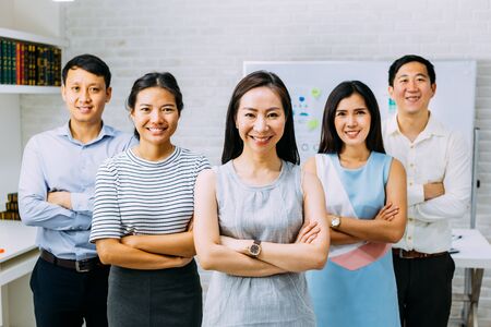 Smiling Asian young business people in casual wear standing in line with arms folded in meeting room. Row of Business men and women looking at cameraの写真素材