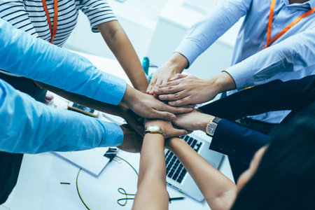 Young Asian business people gathering and putting hands together in meeting room. Business men showing unity and collaboration gesture.の写真素材