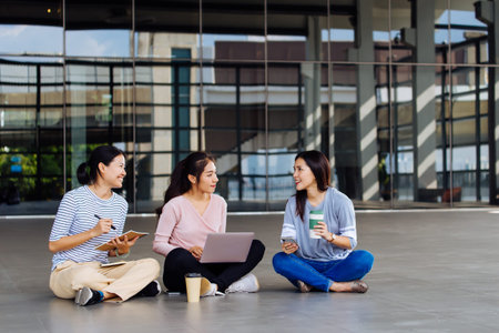 Group of young smart Asian students laughing making notes looking at laptop and discussing while...
