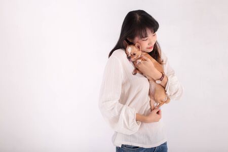 Young Asian female embracing adorable Chihuahua dog and closing eyes while standing against white backgroundの写真素材