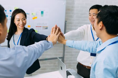 Young Asian business people gathering and putting hands together in meeting room. Business men showing unity and collaboration gesture.の写真素材