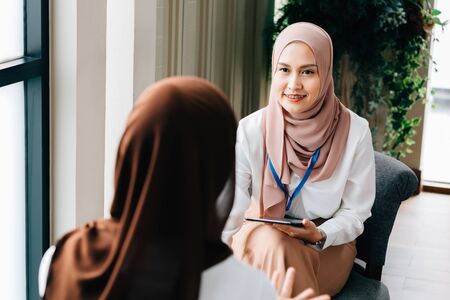 Asian female in hijab holding tablet and speaking with Muslim business partner while working in modern corporate officeの写真素材