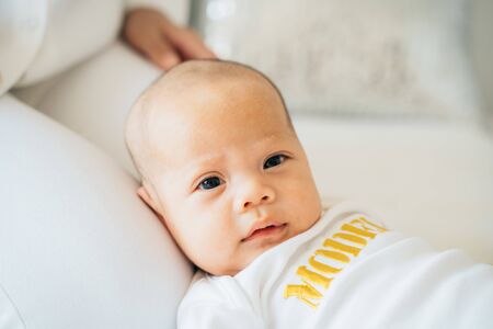Closeup of calm adorable Asian toddler lying on lap of mother in bedroom of flat looking at cameraの写真素材