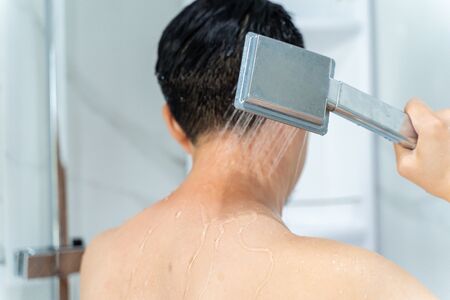 Back view of black haired undressed man pouring hot water from shower head in modern bathroomの写真素材