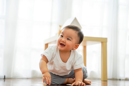 One lovely male infant laughing and having fun in living room against white windows. He can sit on...