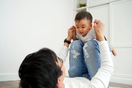 Joyful Asian boy playing airplane with parenting dad in the living room at home. Father is carrying...