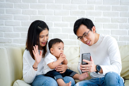 Happy Asian family making a video call at home. Father and mother and son waving at the caller