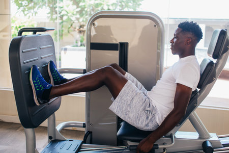 Side view of tired African American man in sportswear listening to music in wireless earphones while...