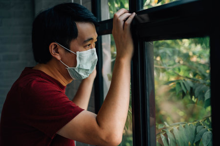 Sick man of coronavirus quarantine looking through the window and wearing a mask for protection...