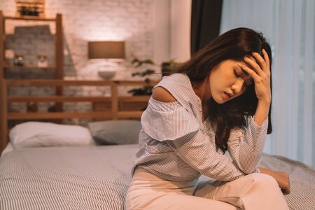 Portrait of 20s young Asian woman suffering pain and medical sickness in bedroom at night. Fever, high temperature, cold, migraine, tiredness, symptoms.の写真素材