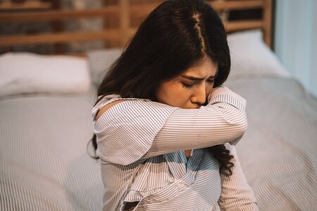 Portrait of 20s young Asian woman having dry cough in bedroom at home. Using elbow as a new normal to prevent pandamic covid-19 from spreading. Coronavirus new normal concept.の写真素材