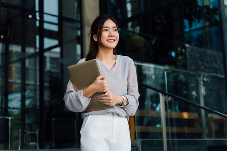One successful and happy young adult business woman holding a laptop with smile. Professional female...