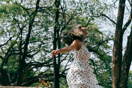 Happy and carefree young 20s woman dancing in the outdoor forest with green trees. Portrait of beautiful and peaceful girl relaxing. Freedom and happiness conceptの写真素材