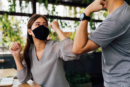 Asian woman and man friends wearing face mask outdoors. Friends greeting and shaking with elbows as...