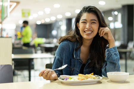 Young Asian woman looking at camera in restaurant eating meal. Beautiful Asia girl smiling in cafeteriaの写真素材