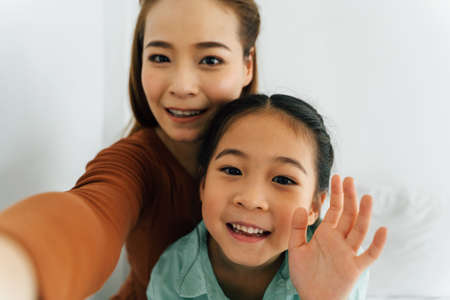 Happy Chinese mother with cute girl waving towards cameraの写真素材