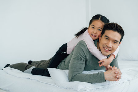 Cheerful Asian girl lying on fathers back looking at camera