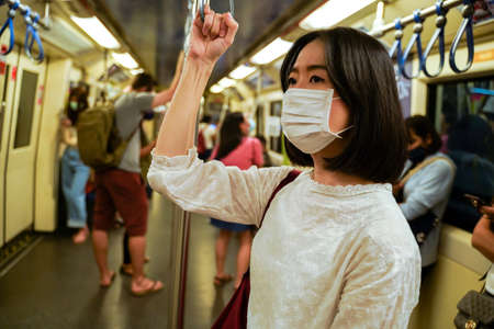 young adult Asian woman wearing a face mask on subway train in Bangkok, Thailand. New normal lifestyle during Covid19 - Coronavirus pandemicの写真素材