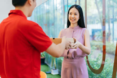 Happy Asian businesswoman taking pizza boxes from pizza delivery man, lunch break, takeaway pizza delivery, food and drinkの写真素材