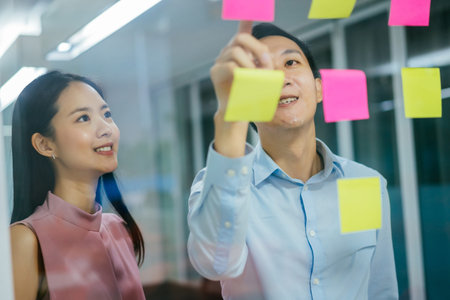 Two business coworkers sticking post notes on glass, planning, strategy, organization