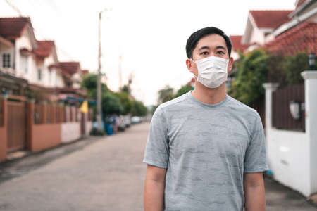 Young Asian man wearing a face protective mask in front of his house outdoors. Wearing a face mask before leaving home.の写真素材