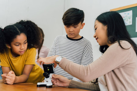 Young woman showing multiethnic children microscope in science class, learning, discovery,...
