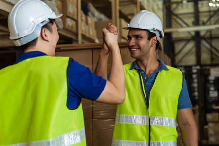 Indian male factory warehouse worker working in logistic industry indoor. Friends greeting and doing handshake with hand grasp inside depotの写真素材