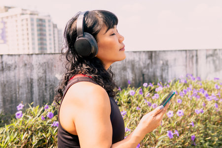Young Asian woman listening to music while exercising in the park. Female sporty jogger using a mobile phone outdoorsの写真素材