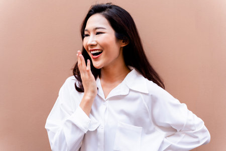 20s young Asian happy millenial woman in white shirt in clean background smiling and laughing confidently with beautiful teeth. Portrait of beauty skin care and oral care conceptの写真素材