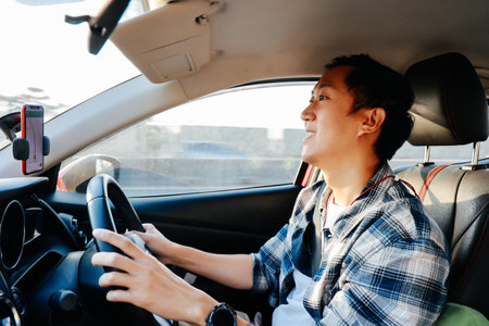 Close-up of Young Asian man smiling and looking at the urban road while driving a car in cityの写真素材